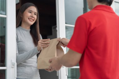 Mutlu gülümseyen Asyalı kadın, kurye evinden bir paket yiyecek alıyor. Teslimatçı ekspres teslimat gönderdi. Çevrimiçi alışveriş, kağıt konteynır, paket servisi, postacı, dağıtım servisi, paketler