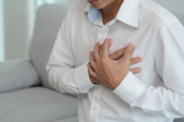 Kalp krizi belirtileriyle el ele tutuşan Asyalı adamın göğüs ağrısı var. Kalp rahatsızlığı, sızıntı, genişleme, genişlemiş kalp, göğsüne acı veren bir ekspresyoyla bastırma.