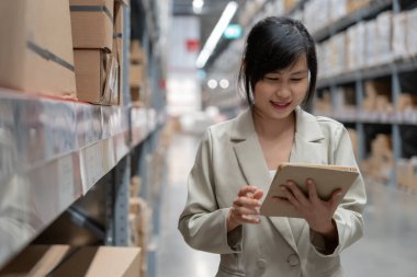 Dijital tablet kullanan bir iş kadını, dağıtım deposu fabrikasında stok ürün envanterini kontrol ediyor. Lojistik ticaret nakliyesi ve teslimatı.