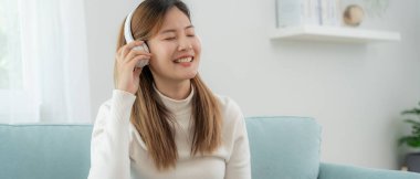 Kablosuz kulaklıklı neşeli genç Asyalı kadınlar oturup müzik dinliyor, eğleniyor, müzik dinliyor, kolunu kaldırıyor, en sevdiği şarkıyla dans ediyor, harika bir soundtrack 'in keyfini çıkarıyor, mutlu bir hayat sürüyor, eğleniyor.