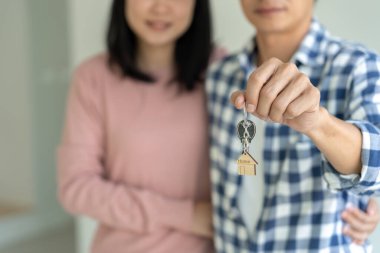 Moving house, relocation. Couple hold key house keychain in new apartment, inside the room was a cardboard box containing personal belongings and furniture. move in the new apartment or condominium