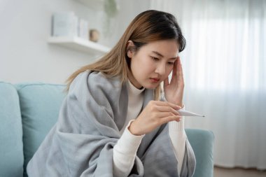 Young Asian woman having high fever while checking body temperature, female sneezing and runny nose with seasonal influenza, allergic, digital thermometer, virus, coronavirus, illness, respiratory