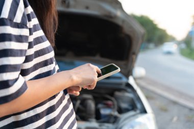 breakdown, broken car, repair. Woman uses mobile phone check insurance premiums through application due to car accident . Find garage to get car fixed during country tour, waiting for help, emergency.