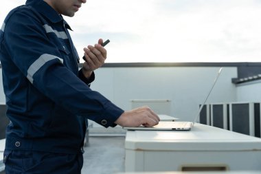 Asian maintenance engineer work on the roof of factory. contractor inspect compressor system and plans installation of air condition systems in construction. technology, walky talky, maintenance