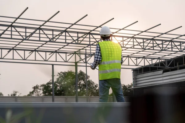 inspector or engineer is inspecting construction and quality assurance new factory using a checklist. Engineers or architects or contactor work to build the factory before handing it over to the homeowner