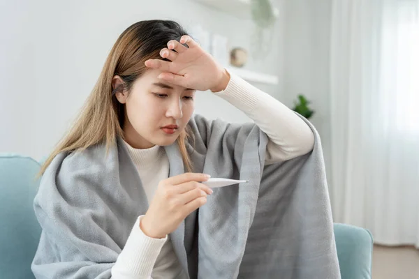 Young Asian woman having high fever while checking body temperature, female sneezing and runny nose with seasonal influenza, allergic, digital thermometer, virus, coronavirus, illness, respirator