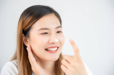Güzel Asyalı kadın gülümsemesi burun derisine krem sürüyor. Sağlıklı bir kadın yüzüne krem sürün ve makyaj yapın. Cilt kremi reklamı, kırışıklık önleyici, bebek yüzü, beyazlatma, nemlendirici, gözenekleri sıkma