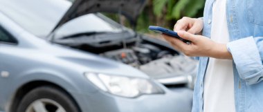 breakdown, broken car, repair. Woman uses mobile phone check insurance premiums through application due to car accident . Find garage to get car fixed during country tour, waiting for help, emergency.