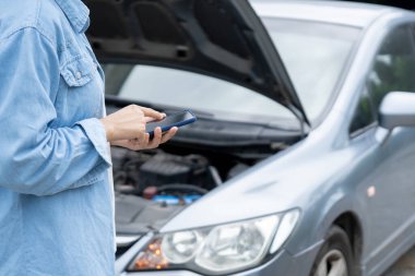 breakdown, broken car, repair. Woman uses mobile phone check insurance premiums through application due to car accident . Find garage to get car fixed during country tour, waiting for help, emergency.