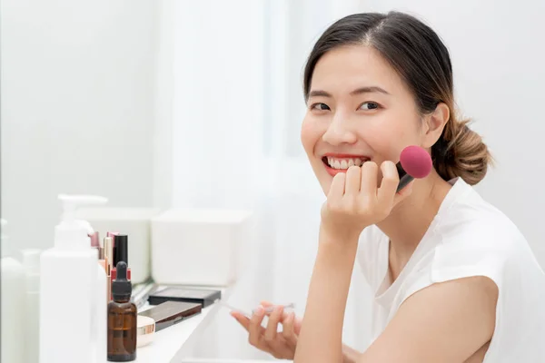 Portrait Beautiful Asian woman sit in front of a mirror and smile on makeup. face of healthy woman apply makeup. Advertisement, lifestyle , cosmetics, makeup accessories, beauty activity, beautician