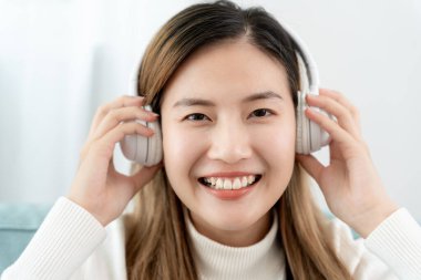 Kablosuz kulaklıklı neşeli genç Asyalı kadınlar oturup müzik dinliyor, eğleniyor, müzik dinliyor, kolunu kaldırıyor, en sevdiği şarkıyla dans ediyor, harika bir soundtrack 'in keyfini çıkarıyor, mutlu bir hayat sürüyor, eğleniyor.