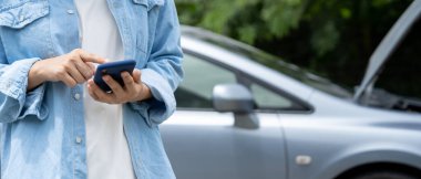 breakdown, broken car, repair. Woman uses mobile phone check insurance premiums through application due to car accident . Find garage to get car fixed during country tour, waiting for help, emergency.