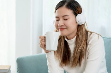 Kablosuz kulaklıklı neşeli genç Asyalı kadınlar oturup müzik dinliyor, eğleniyor, müzik dinliyor, kolunu kaldırıyor, en sevdiği şarkıyla dans ediyor, harika bir soundtrack 'in keyfini çıkarıyor, mutlu bir hayat sürüyor, eğleniyor.