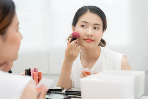 Portrait Beautiful Asian woman sit in front of a mirror and smile on makeup. face of healthy woman apply makeup. Advertisement, lifestyle , cosmetics, makeup accessories, beauty activity, beautician