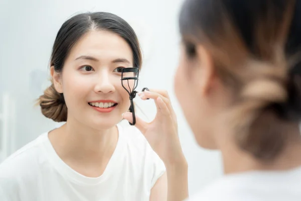 Beautiful Asian woman sit in front of a mirror smile and curling eyelashes. face of a healthy woman applying makeup. Advertisement, lifestyle , cosmetics, accessories, beauty activity, beautician