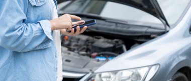breakdown, broken car, repair. Woman uses mobile phone check insurance premiums through application due to car accident . Find garage to get car fixed during country tour, waiting for help, emergency.