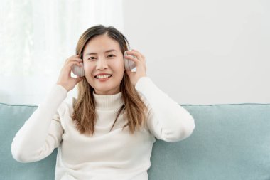 Kablosuz kulaklıklı neşeli genç Asyalı kadınlar oturup müzik dinliyor, eğleniyor, müzik dinliyor, kolunu kaldırıyor, en sevdiği şarkıyla dans ediyor, harika bir soundtrack 'in keyfini çıkarıyor, mutlu bir hayat sürüyor, eğleniyor.