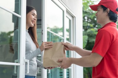 Mutlu gülümseyen Asyalı kadın, kurye evinden bir paket yiyecek alıyor. Teslimatçı ekspres teslimat gönderdi. Çevrimiçi alışveriş, kağıt konteynır, paket servisi, postacı, dağıtım servisi, paketler