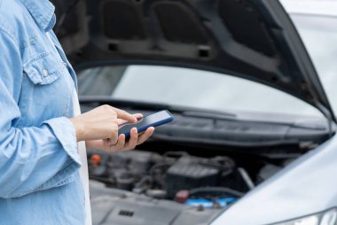 breakdown, broken car, repair. Woman uses mobile phone check insurance premiums through application due to car accident . Find garage to get car fixed during country tour, waiting for help, emergency
