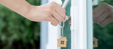 Evin kilidini açmak için ev sahibi anahtarı kapıya takılı. Kira ve satış için ikinci el ev. Sahibi yeni ev, satın al, sat, yenile, yatırım, sahip, mülk