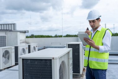 Asian maintenance engineer work on the roof of factory. contractor inspect compressor system and plans installation of air condition systems in construction. technology, walky talky, maintenance
