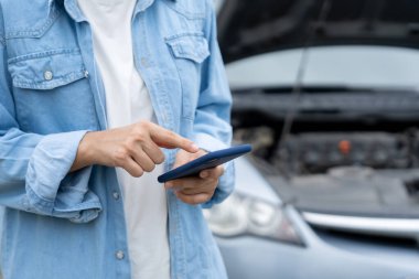 breakdown, broken car, repair. Woman uses mobile phone check insurance premiums through application due to car accident . Find garage to get car fixed during country tour, waiting for help, emergency