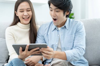 Gülümseyen Asyalı çift internet alışverişinde akıllı telefon kullanıyor. Koca, güzel bir eş için doğum günü hediyesi ödemeye hazır. Balayı için internetten konaklama, uygulama, uçak biletleri..