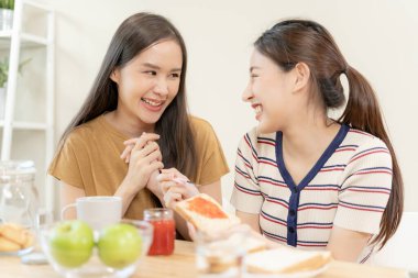 LGBT. Asyalı lezbiyen çift evde kahvaltı ederken gülümsüyor ve sevgi gösteriyor. Genç Asyalı çift birbirlerine mutlu bir şekilde sarılıyorlar, aşıklar, homoseksüellik, eşcinsellik, özgürlük, ifadeler.