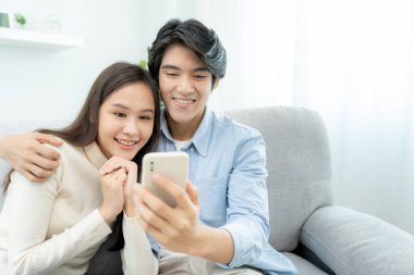 Gülümseyen Asyalı çift internet alışverişinde akıllı telefon kullanıyor. Koca, güzel bir eş için doğum günü hediyesi ödemeye hazır. Balayı için internetten konaklama, uygulama, uçak biletleri..