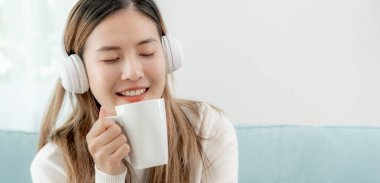 Kablosuz kulaklıklı neşeli genç Asyalı kadınlar oturup müzik dinliyor, eğleniyor, müzik dinliyor, kolunu kaldırıyor, en sevdiği şarkıyla dans ediyor, harika bir soundtrack 'in keyfini çıkarıyor, mutlu bir hayat sürüyor, eğleniyor.