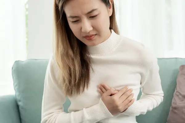 hand hold chest with heart attack symptoms, asian woman have chest pain caused by heart disease, leak, dilatation, enlarged coronary heart, press on the chest with a painful expressio