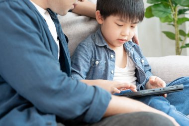 Küçük çocukla tablet kullanarak öğretmencilik oynayan mutlu bekar baba. Aile evde mutlu ve heyecanlı. Baba oğul birlikte vakit geçiriyorlar, iyi baba, bağımlılık düzelt, kontrol et.