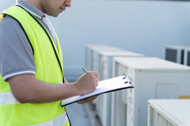 Asyalı bakım mühendisi fabrikanın çatısında çalışıyor. Müteahhit kompresör sistemini denetleyecek ve inşaatta havalandırma sistemi kurmayı planlıyor. Kontrol listesi, müfettiş, kontrol