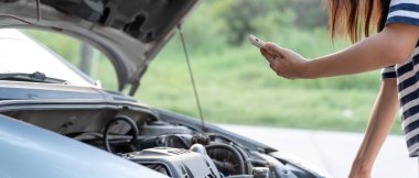 breakdown, broken car, repair. Woman uses mobile phone check insurance premiums through application due to car accident . Find garage to get car fixed during country tour, waiting for help, emergency.