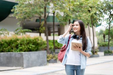 Sırt çantalı ve tabletli güzel Asyalı öğrenci. Üniversite kampüsünde kitap taşımaktan mutlu gülümseyen kız. Uluslararası Asya Üniversitesi 'nde kadın portresi. Eğitim, eğitim, okul