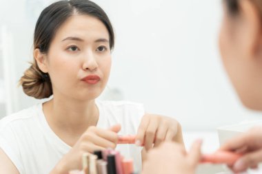 Güzel bir Asyalı kadın aynanın karşısına oturur ve makyaja gülümser. Makyaj yapan sağlıklı bir kadının yüzü. Reklam, yaşam tarzı, kozmetik, makyaj malzemeleri, güzellik etkinliği, güzellik uzmanı.