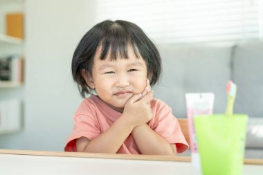 Küçük Asyalı kız yanak yanağa bastırıyor, diş ağrısı çekiyor. Diş çürümesi, diş problemleri, çocuk duyguları ve yüz ifadesi, ağız sağlığı, şekerlerin azaltılması, florin kaplama