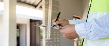 inspector or engineer is inspecting construction and quality assurance new house using a checklist. Engineers or architects or contactor work to build the house before handing it over to the homeowne