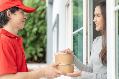 Happy smiling Asian woman receives paper box parcel of food from courier front house. Delivery man send deliver express. online shopping, paper container, takeaway, postman, delivery service, packages