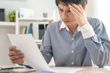 Yüklü faturaları ve faturaları olan stresli ve baş ağrısı çeken Asyalı bir adamın harcamaları ve kredi kartı borçlarını ödeyecek parası yok. kıtlık, mali sorunlar, mortgage, kredi, iflas, iflas, yoksul, boş duvar