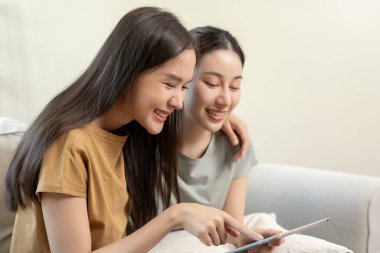 LGBT grubu. Güzel görünümlü lezbiyen çiftler tatilde evde tablet kullanır. Asyalı genç çift birbirlerine mutlu bir şekilde sarılıyorlar, aşık, biseksüellik, homoseksüellik, özgürlük, ifade, mutlu hayat.
