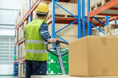 Depo işçisi, envanterdeki malları inceledikten sonra palet kamyonunu çekiyor ve stok ürünlerini kontrol ediyor. Lojistik ticaret nakliyesi ve müşterilere teslimat. Denetleme, depo, depo, fabrika