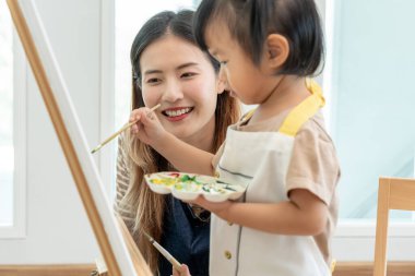 Mutlu Asyalı anne küçük kız için boya öğreniyor. Aile evde mutlu ve heyecanlı. Anne ve kızı birlikte vakit geçiriyorlar. Tatil, Faaliyet, Yönetici Fonksiyonu, IQ, EQ