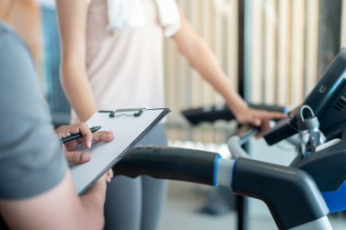 Kadın koşu bandında koşuyor, antrenör kayıtları ve antrenörler için tavsiyeler ve nasıl egzersiz yapılacağını kontrol ediyor. Doğru egzersiz. diyet, vücut şekli, sağlıklı, güçlü, bakım, spor salonu, fitness, tatil