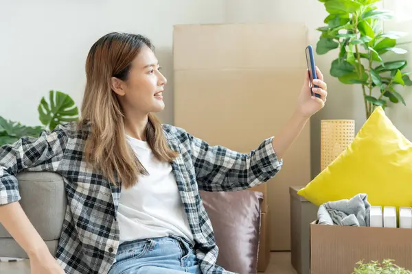 Taşınmak, taşınmak. Asyalı bir kadın kendini iyi hisseder, dinlenir ve yeni evde telefon kullanır. Odanın içinde kişisel eşyaları ve mobilyaları içeren bir karton kutu vardı. kondominiu içinde taşı