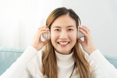 Kablosuz kulaklıklı neşeli genç Asyalı kadınlar oturup müzik dinliyor, eğleniyor, müzik dinliyor, kolunu kaldırıyor, en sevdiği şarkıyla dans ediyor, harika bir soundtrack 'in keyfini çıkarıyor, mutlu bir hayat sürüyor, eğleniyor.