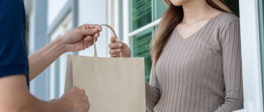 Mutlu gülümseyen Asyalı kadın, kurye evinden bir paket yiyecek alıyor. Teslimatçı ekspres teslimat gönderdi. Çevrimiçi alışveriş, kağıt konteynır, paket servisi, postacı, dağıtım servisi, paketler