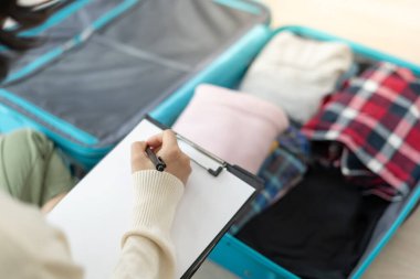 Seyahat çantası. Kadın, kontrol listesi tarafından yolculuk sırasında kullanılan eşyaların sayısını ve detaylarını kontrol ediyor. Genç kadınlar giysi ve kişisel eşyalardır. Yolculuktan önce bavullarınızı hazırlayın.