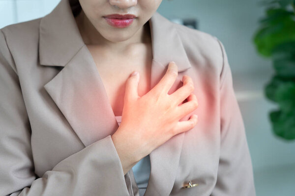 рука держать грудь с симптомами сердечного приступа, азиатская женщина упорно работают есть боли в груди, вызванные болезнью сердца, утечка, расширение, увеличенное коронарное сердце, нажмите на грудь с болезненным выражением