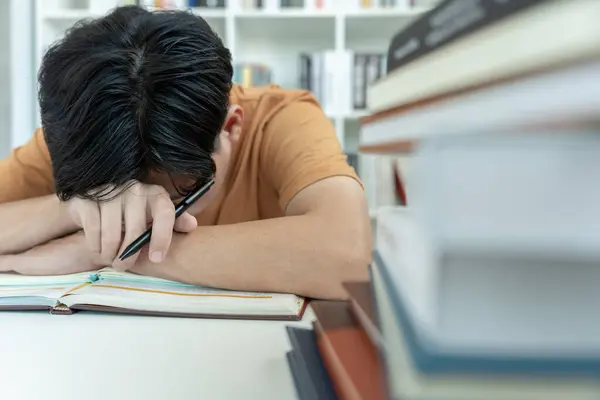 Asyalı öğrenci sınavlar yüzünden endişeli. Erkek öğrenci kütüphanede sınav ve öğrenme derslerine hazırlanıyor. Stres, umutsuzluk, acele, yanlış anlama okuma, cesaret kaybı, beklenti, bilgi, yorgunluk